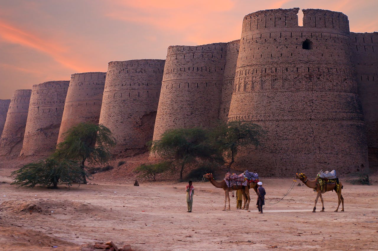Scenic view of Derawar Forts towers at sunset in the Punjab desert with camels and people.